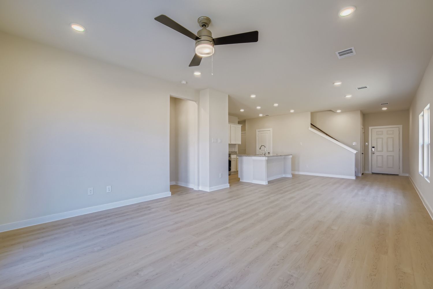A large empty room with a wood floor and a ceiling fan.