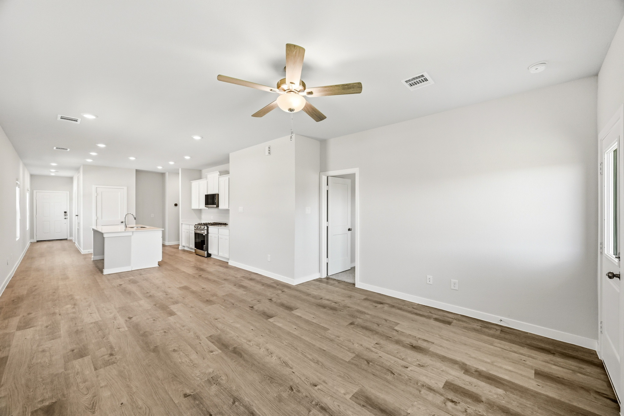A large empty room with a ceiling fan and white cabinets.