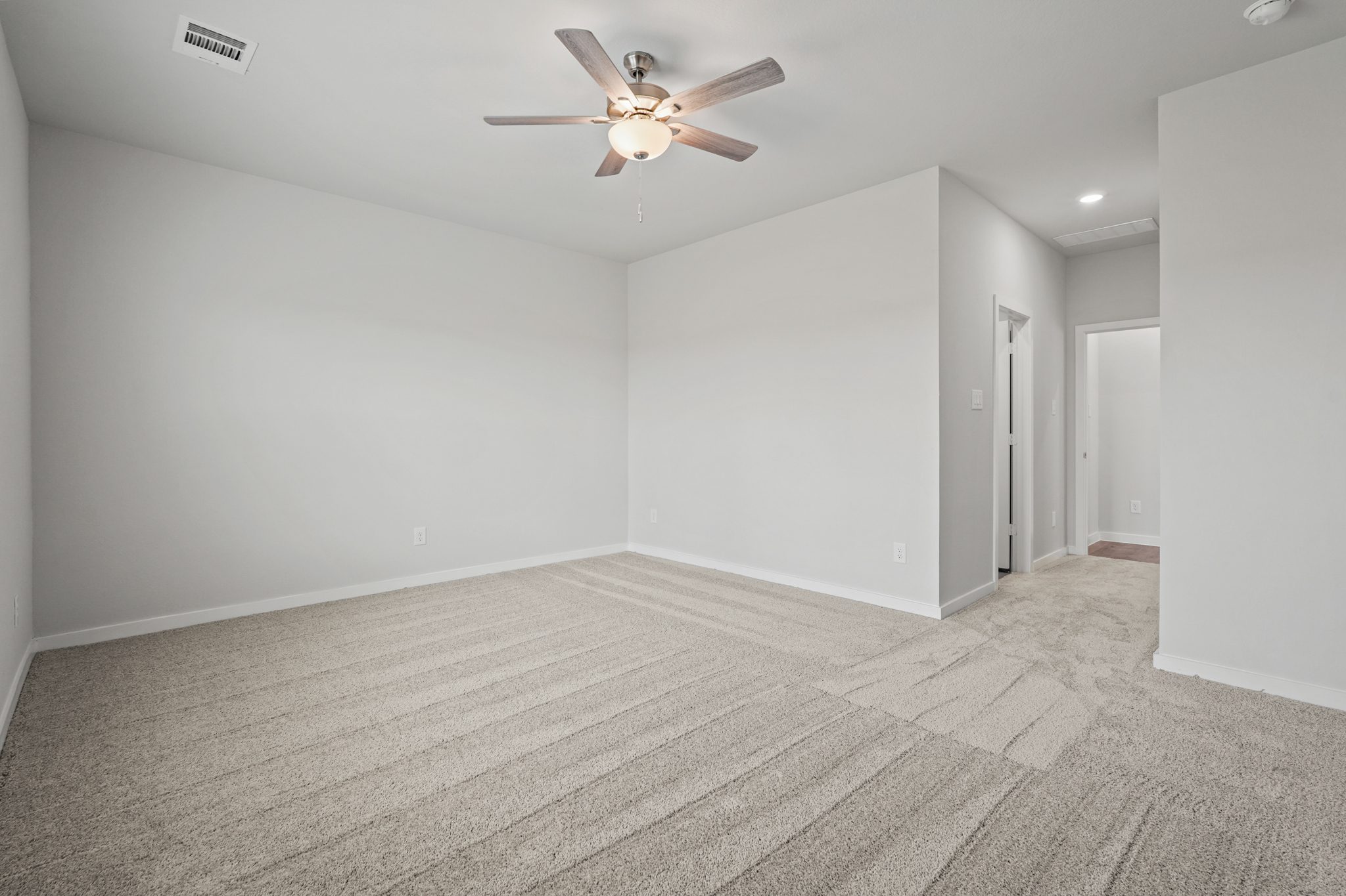 A room with a ceiling fan and a carpet.