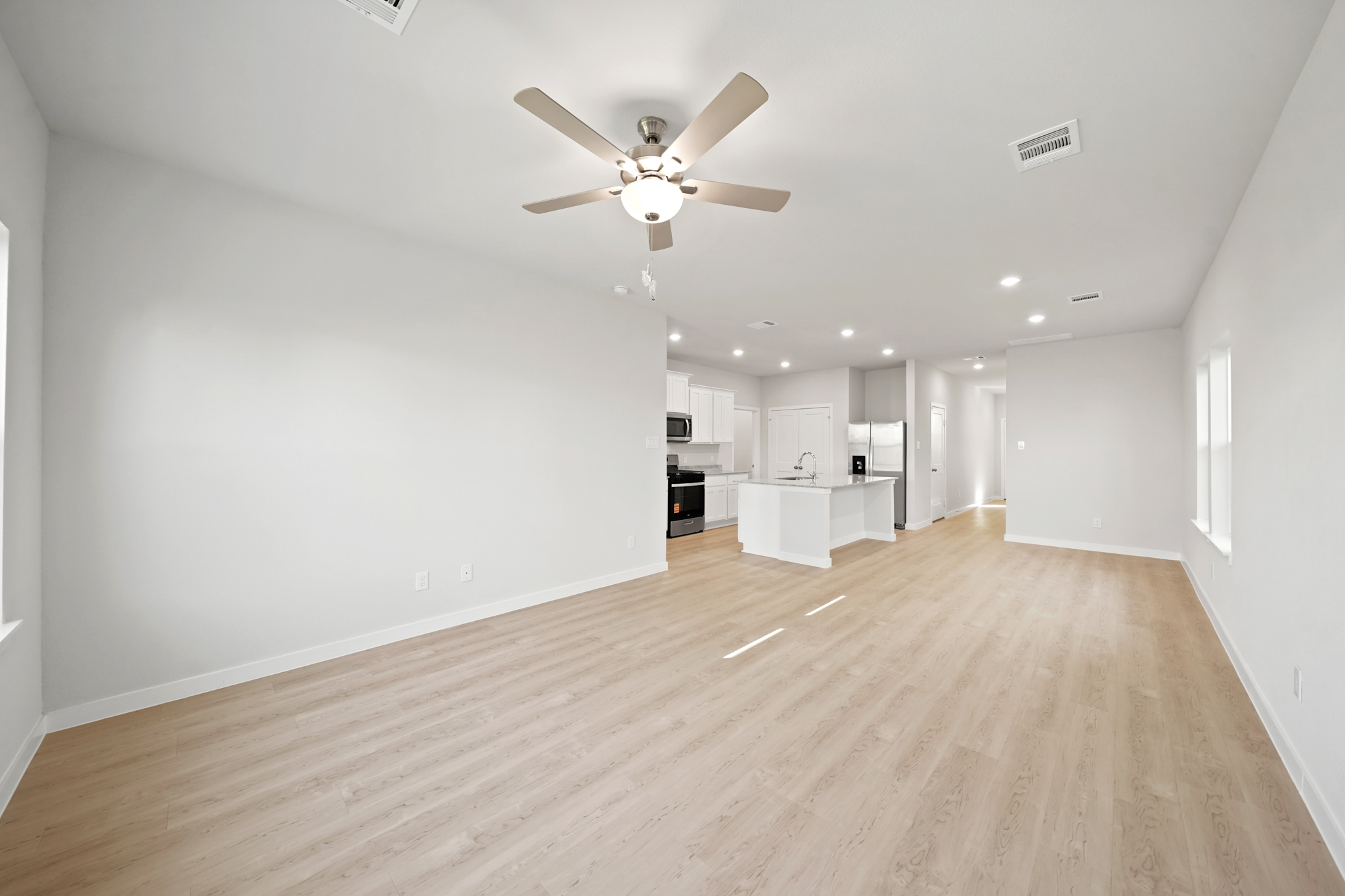 A large empty room with a ceiling fan and a wood floor.