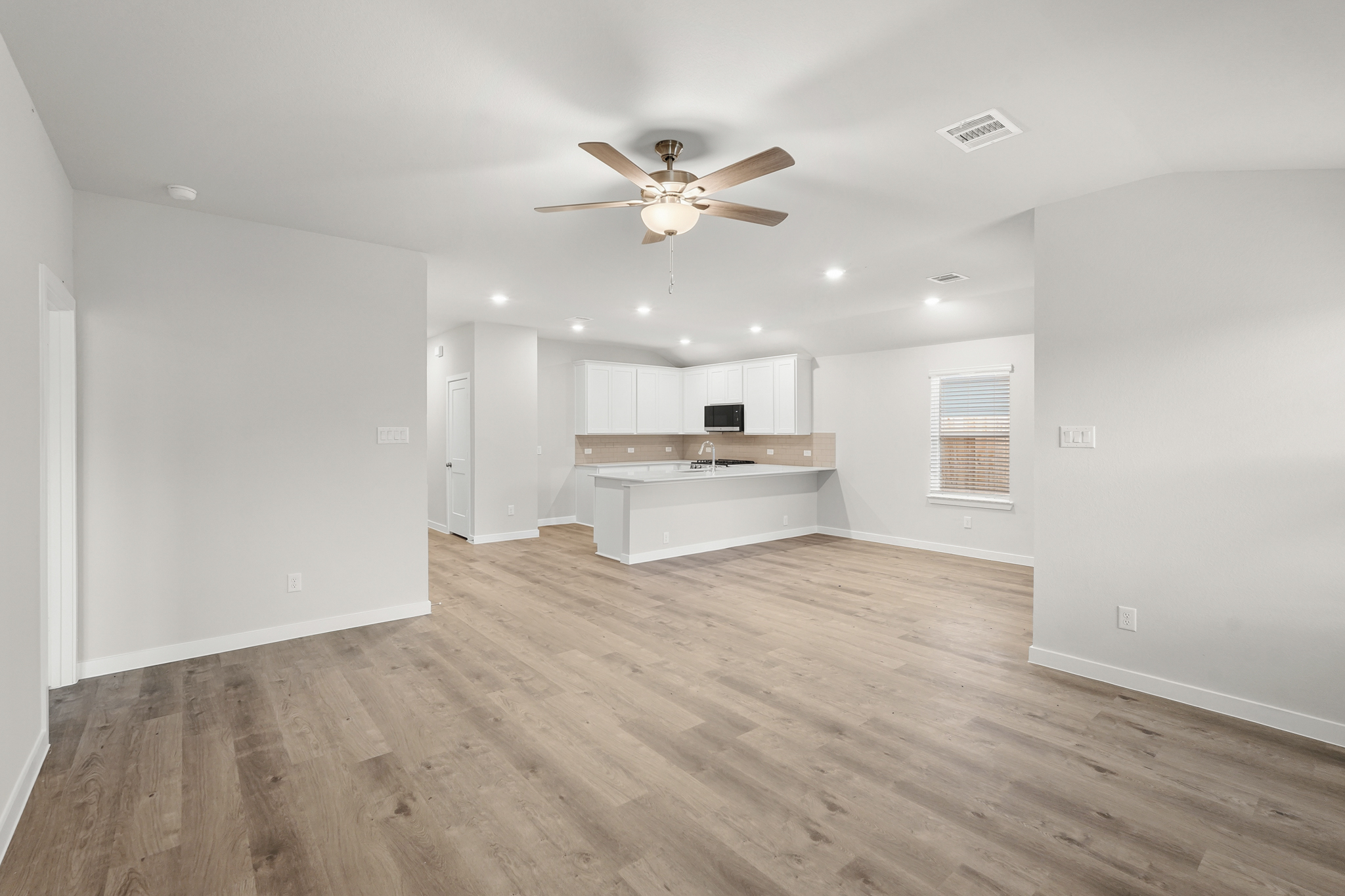 A large empty room with a wood floor and a ceiling fan.