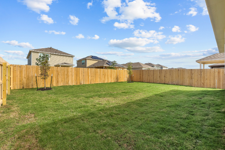 A fenced in yard with a tree and a house in the background.
